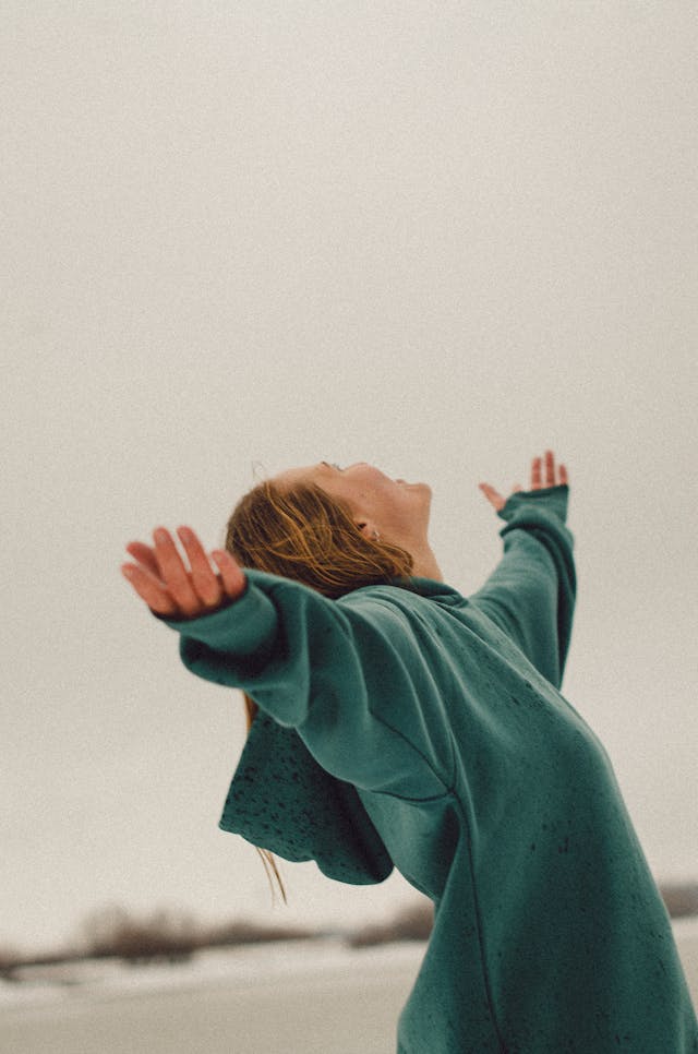 woman in green sweatshirt with arms spread